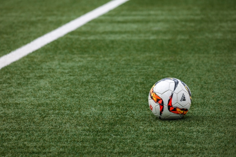 Ein Fußball mit rot-gelbem Muster liegt auf einem grünen Kunstrasenplatz nahe einer weißen Begrenzungslinie, bereit für das nächste Spiel des SV-Waldwimmersbach.
